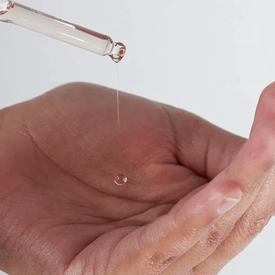 Een model gebruikt een pipet van een Medik8 serum en laat druppels in haar hand vallen voor huidverzorging.