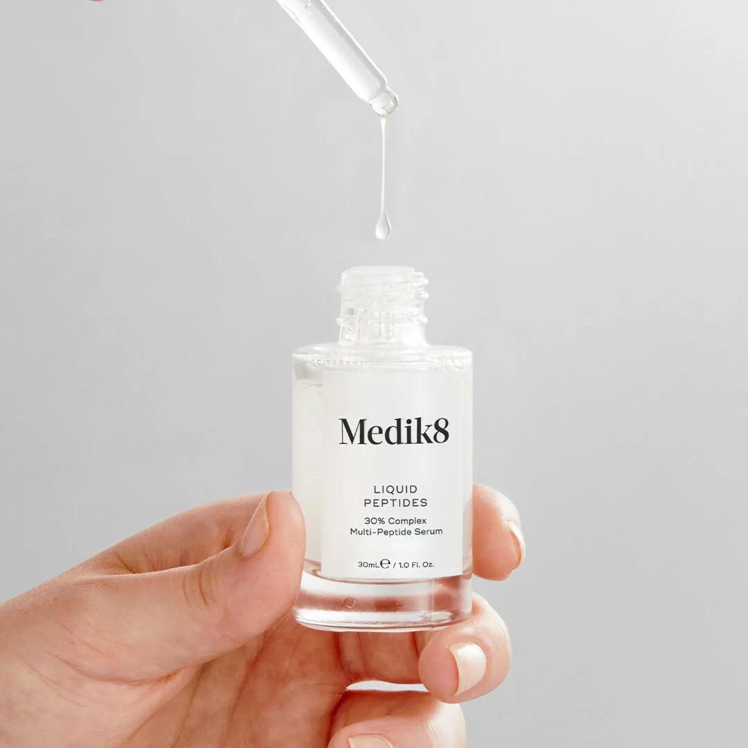 Een model houdt in haar handen een flesje Medik8 Liquid Peptides 30ml en laat de pipet uit het serum komen terwijl het terugdruppelt in het flesje.